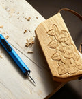 Blue mini cordless engraving pen with LED display beside a carved wooden plaque
