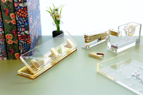 Clear Acrylic 3 Hole Punch For 10 Sheets With Four And A Quarter Inch Hole Spacing Gold Accents on a desk with office supplies
