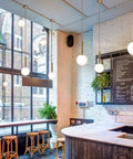 Modern Globe Pendant Light for Kitchen Island White Milk Glass with Brass Finish in café setting.