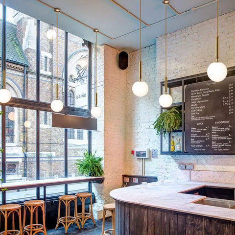 Modern Globe Pendant Light for Kitchen Island White Milk Glass with Brass Finish in café setting.