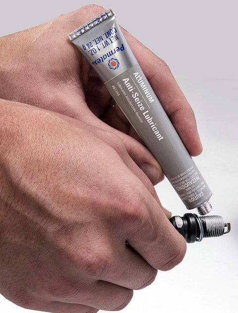 Person applying Anti Seize Lubricant 81343 1 Oz Tube Four Pack With Aluminum Copper And Graphite Blend Salt And Moisture Resistant Marine Grade Formula For No Fuss Spark Plug Removal, Cylinder Head Bolts, And Quick Disassembly to a spark plug.