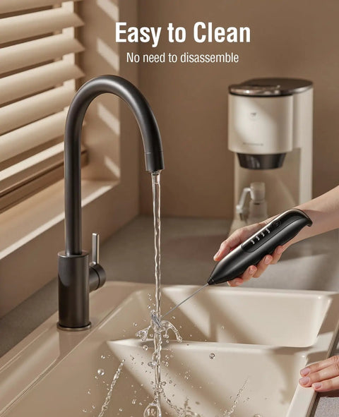 Rechargeable Electric Milk Frother Handheld 3 In 1 with LED Display being rinsed under a faucet in a kitchen setting