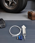 Top Notch Manual Automotive Fluid Extractor Pump For Oil Changes And Brake Fluid Service With Durable Plastic Build Plus Long Extension Tubes For Easy Car Care DIY Jobs on garage floor with tools and a tire.