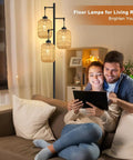 Couple using tablet beside Boho Rattan Tree Floor Lamp With Three Edison Bulbs, Industrial Black Standing Farmhouse Style lamp.
