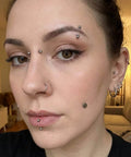 Person with multiple facial and ear piercings featuring nose, lip, and eyebrow jewelry in a living room setting.