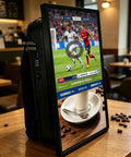 Rugged Mobile Ad Backpack With Kickass 21 Inch HD LCD Display showing sports video in a cafe setting on a wooden table.