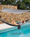 Person relaxing in Heavy Duty Camping Hammock With Rain Fly Tarp And Mosquito Net 440 Lb Capacity Portable Tree Hammock by a pool.