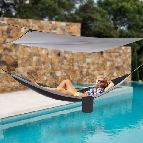 Person relaxing in Heavy Duty Camping Hammock With Rain Fly Tarp And Mosquito Net 440 Lb Capacity Portable Tree Hammock by a pool.