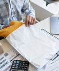 Person packing shirt into 200 Pack Poly Mailers With Four Assorted Sizes 10 By 6 Inches, 11.8 By 7.8 Inches, 13.7 By 9.8 Inches, And 16.6 By 11.4 Inches Waterproof Tear Resistant White Shipping Envelopes For Clothes Books And More