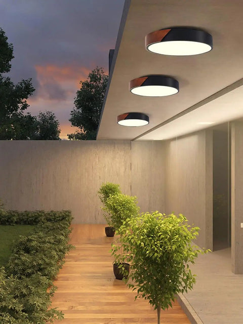 Outdoor view of Slick Modern Black Wood Look Flush Mount Ceiling Light 3 Light Fixture illuminating a patio at dusk.