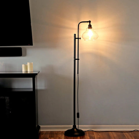 Tall Industrial LED Floor Lamp With Adjustable Head And Rustic Glass Teardrop Shade, Black Finish, in living room corner.