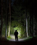 Silhouette of a person in a forest illuminated by Flateye High Performance Flashlight With Cree LED Multi Position Beam Waterproof And Shockproof 1700 Lumens Your Go To Tool For Trails Work Sites Emergencies And Everyday Outdoor Adventures