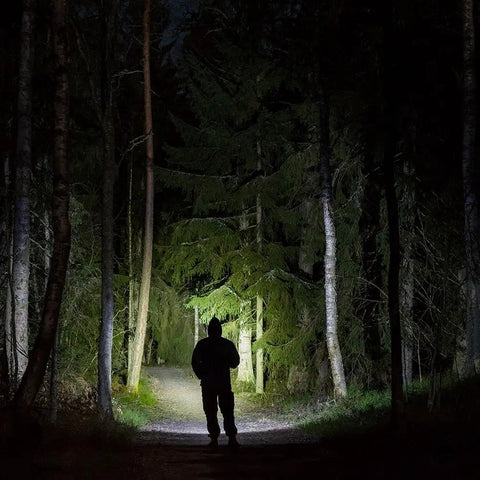 Silhouette of a person in a forest illuminated by Flateye High Performance Flashlight With Cree LED Multi Position Beam Waterproof And Shockproof 1700 Lumens Your Go To Tool For Trails Work Sites Emergencies And Everyday Outdoor Adventures