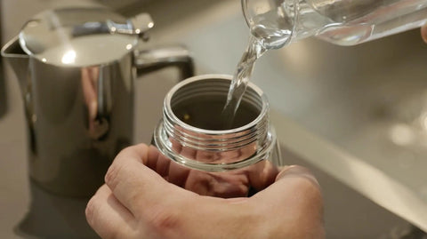 Pouring water into the Hella Durable Stainless Steel Stovetop Espresso Maker for rich coffee brews in a kitchen setting.