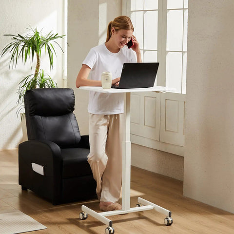 Person using Small Standing Desk On Wheels With Adjustable Height Portable Laptop PC Table For Home Office Sit Stand Workstation 19 Inch Wide Modern White Lockable Mobile Rolling Desk With Pneumatic Height Adjustment For Sit Standing Flex Office Setup Effortless next to a black chair in a home office.