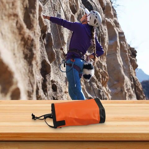 Orange 5L Rope Storage Pouch With Quick Draw Tower for rock climbing on wooden table, climber scaling rock face in background.