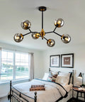 Six Light Glass Globe Chandelier With Adjustable Boom in gold and black hanging over a bed in a bright room.