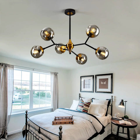 Six Light Glass Globe Chandelier With Adjustable Boom in gold and black hanging over a bed in a bright room.