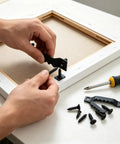 Person installing a 50 Pack Small Sawtooth Picture Hangers With Screws, Black Steel Hanging Hardware Kit for secure wall mounting.