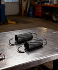 Pair Of Heavy Duty Steel Recliner Springs Featuring Half Inch Tension Coils on a workbench, ideal for furniture fixes.