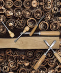 Heavy Duty 16 Piece Wood Carving Tool Set With Premium Handles Sharp Chisels And Gouges Includes Wooden Mallet And Whetstone For Absolutely Kickass Detail Craftsmanship on wooden surface with curled shavings.