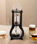 Kick Back And Sip Smooth Chills With This Sharp Cold Brew Drip Coffee Maker Crafted From A Borosilicate Pitcher And Real Wood Stand For Hassle Free Iced Coffee Runs That Come Out Fresh And Totally On Point Daily, showing cold brew coffee maker with borosilicate glass and wooden stand.