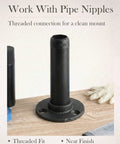 Industrial steampunk style 1/2 inch black iron pipe flange with threaded pipe nipple connection on a wooden surface.