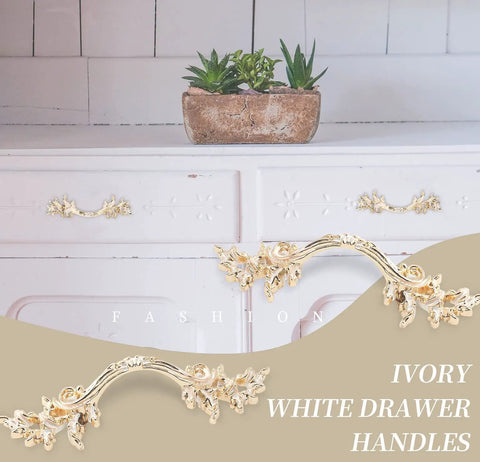 Ivory white drawer handles installed on a vintage dresser, with decorative floral design and gold accents, front view.