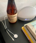 Nightstand with brown bottle, digital clock, books, and white charging cable organized with adhesive clip.