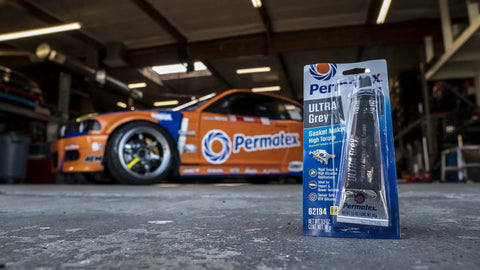 Ultra Grey RTV Silicone Gasket Maker 3 oz package in an automotive garage with a race car in the background.