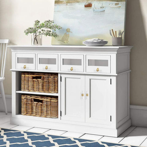 White cabinet with wicker baskets and four drawers, adorned with gold-tone knobs, in a coastal-themed room.