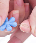 Close-up of hands using blue flower head wire loop from 30 Piece Needle Threader Set With Clear Box Multicolor Flower Head Wire Loop Threaders.