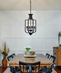 Dining room featuring a 10.63 Inch Black Farmhouse Chandelier With Four Lights Modern Industrial Lantern Pendant Light Fixture For Dining Room Kitchen Foyer Or Hallway Rustic Metal Cage Adjustable E12 Base For A Cozy Home Vibe, above a wooden table with black chairs.