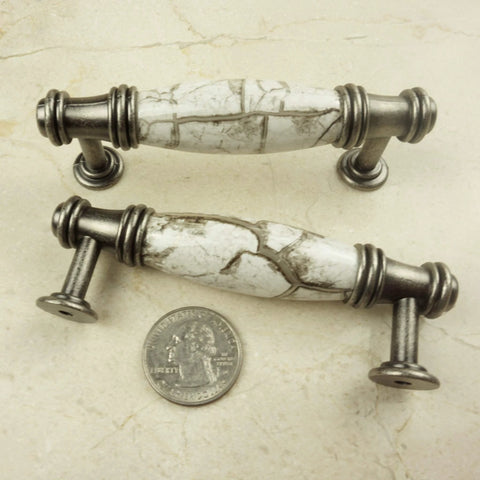 Two decorative cabinet pulls with marble-look design and silver hardware next to a quarter for scale.