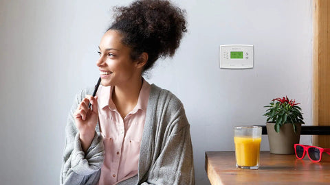 Woman sitting near 7 Day Programmable Thermostat With Backlit Digital Display And Precise Temperature Control To Within 1 Degree Fahrenheit