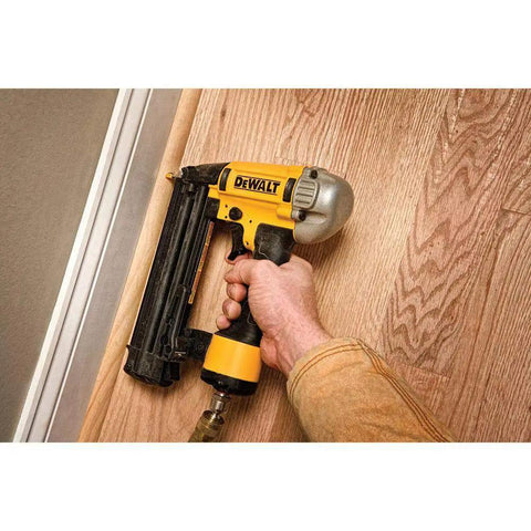 Professional 18 Gauge Brad Nailer With Rear Exhaust Blasts Dust Away, used for trim work, gripped in hand against wood.