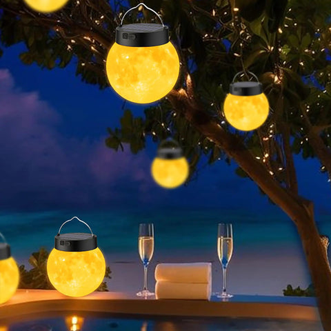 Lit 3D Moon Globe Solar Garden Lights 2 Pack With Warm White LEDs hanging in a tree by a poolside at night.
