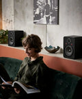Bluetooth Bookshelf Speakers for Turntable With 60W RMS Power on shelf next to person reading, enhancing home entertainment space.