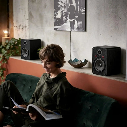 Bluetooth Bookshelf Speakers for Turntable With 60W RMS Power on shelf next to person reading, enhancing home entertainment space.