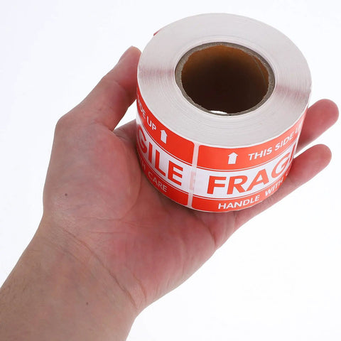 Person holding roll of Fragile Red Shipping Labels With High Visibility And Strong Adhesive, Paper Warning Stickers On Rolls For Small Business Packaging