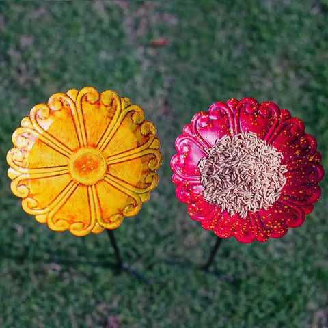 Top view of flower-shaped metal bird baths with seeds on grass, part of the Flower Bird Bath With Metal Stake Set Of Four For Outdoor Gardens A Charming Yard Decor For Bird Lovers Each Bath Measures 7.1 Inches In Diameter And 1.3 Inches Deep With Easy To Install Stakes.