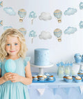 Child holding balloon with Blue Hot Air Balloon Banner Set For Baby Shower And Birthday Party Adventure Awaits Garland in background
