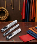 Three-Piece Grommet Hole Punch Set For Leatherworking, Heavy Duty Steel Hollow Punches on leather surface with fabric rolls nearby.