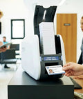 Heavy Duty Id Card Printer Kit Featuring Slick Edge To Edge Color Duplex Prints And Bulletproof Metal Frame Field Upgradeable To Lamination Plus Optional Magstripe Or Contactless Smart Encoding For Boss Level Employee Badges being used at a reception desk.
