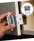 Front view of a silver self-closing inset cabinet hinge held by hand beside a light wood cabinet door