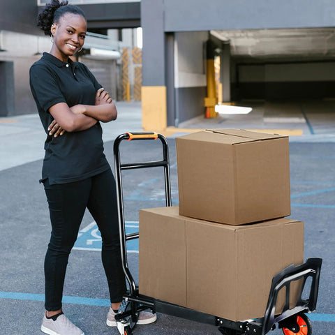 Folding hand truck with black steel frame and orange handle, beside two cardboard boxes in a parking area