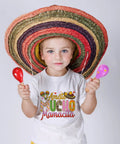 Child in sombrero with maracas wearing Cinco de Mayo themed t-shirt for DIY crafts and festive apparel