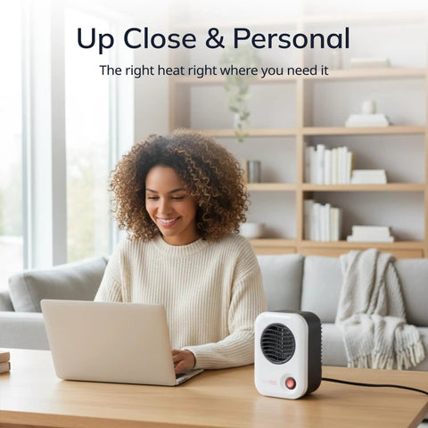 Woman using laptop with MyHeat Personal Space Heater Under Desk, Compact White, 200 Watt Office Foot Warmer on a desk in a cozy room.