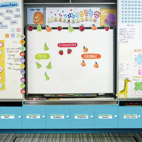 Classroom whiteboard with fruit illustrations and vocabulary words, surrounded by educational materials and colorful decorations.