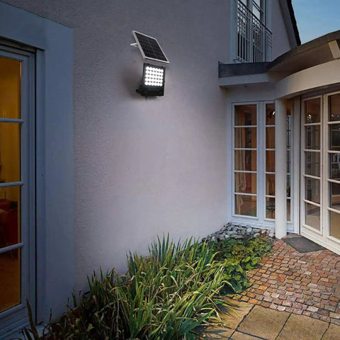 JUDYSSY Solar Flood Lights Led Solar Floodlight mounted on a wall, outdoor waterproof IP65, illuminating garden pathway.